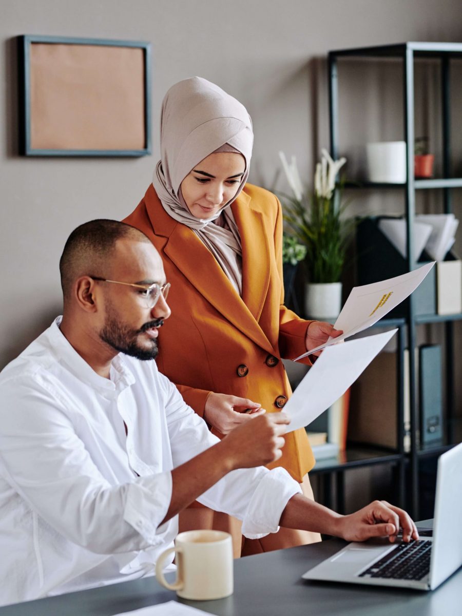 young-secretary-hijab-orange-jacket-consulting-with-her-male-colleague (1) (1) (1)